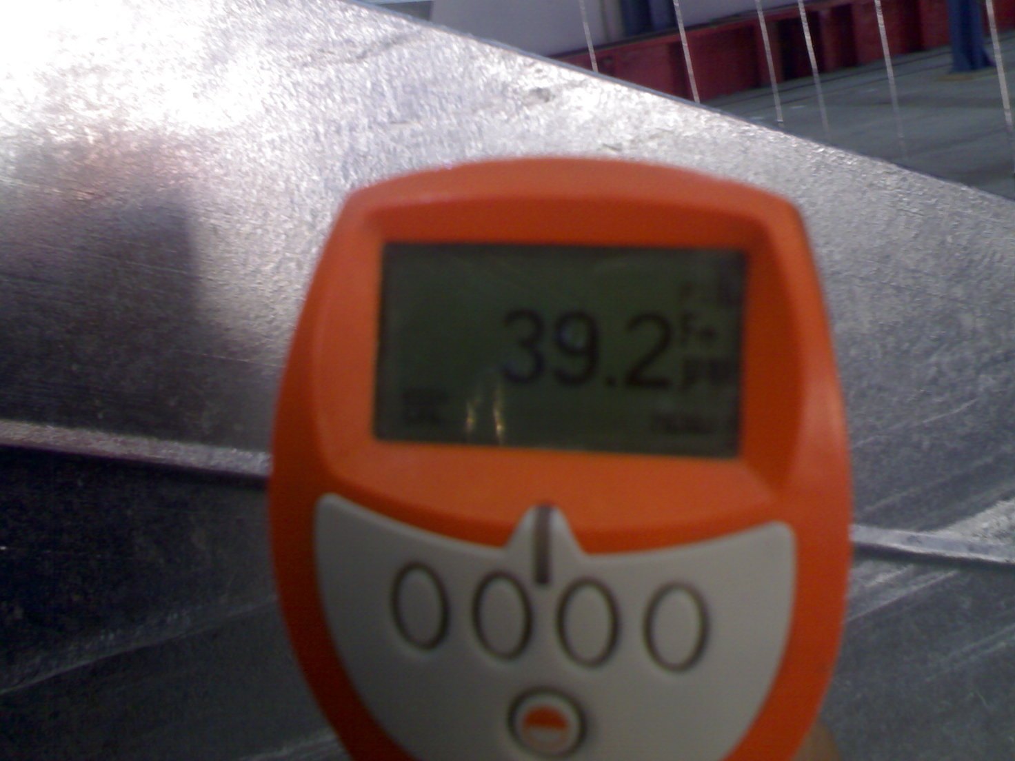 A handheld coating-thickness gauge held probe-down against a bright galvanized folded steel section, its display reading 39.2 — the coating looks completely normal to the eye