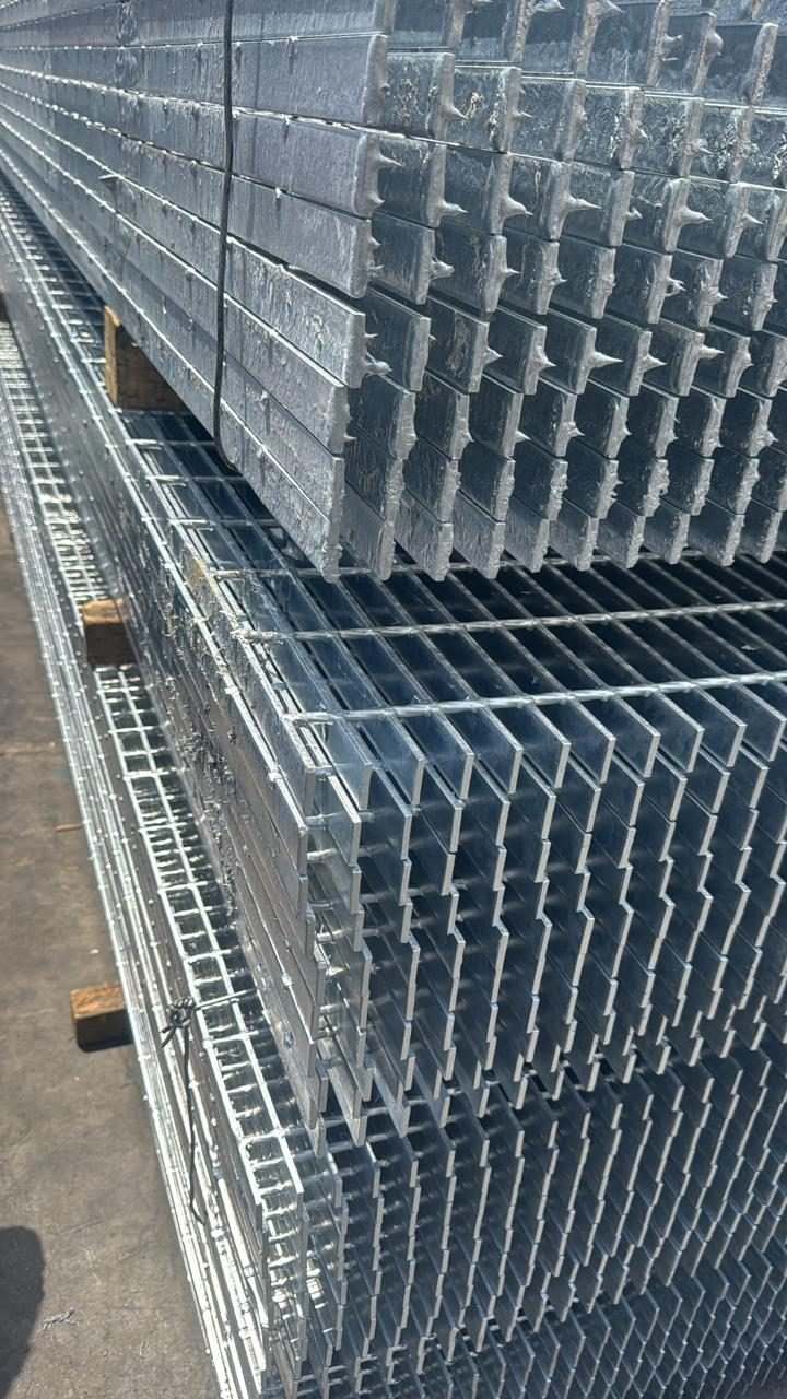 Stacked galvanized gratings seen end-on, with solidified zinc hanging in rows of small icicles from the bearing bar ends
